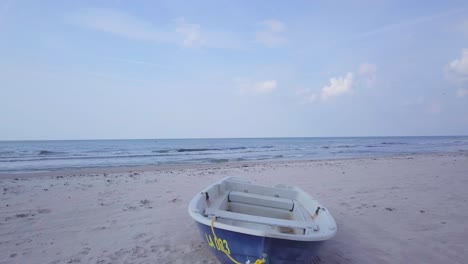 Aerial-view-of-Baltic-sea-coast-on-a-sunny-day,-blue-coastal-fisherman-boat-on-white-sand-seashore-dunes,-coastal-erosion,-climate-changes,-wide-angle-drone-shot-moving-forward-low-1