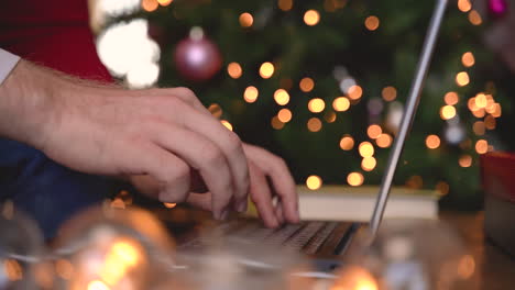 close up view of man hands typing on laptop sitting near the christmas tree in living room with christmas decoration 2