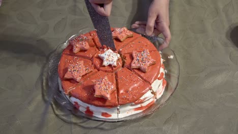 una mujer adulta rodeada de niños corta un hermoso pastel redondo decorado con glaseado rojo en pedazos con un gran cuchillo de cocina. el concepto de una celebración familiar. primer plano. sin rostro. vista superior. 4k