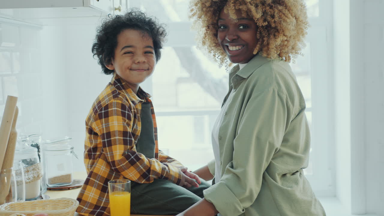 African American Mother Showing Little Son How to Use Smartphone in Kitchen