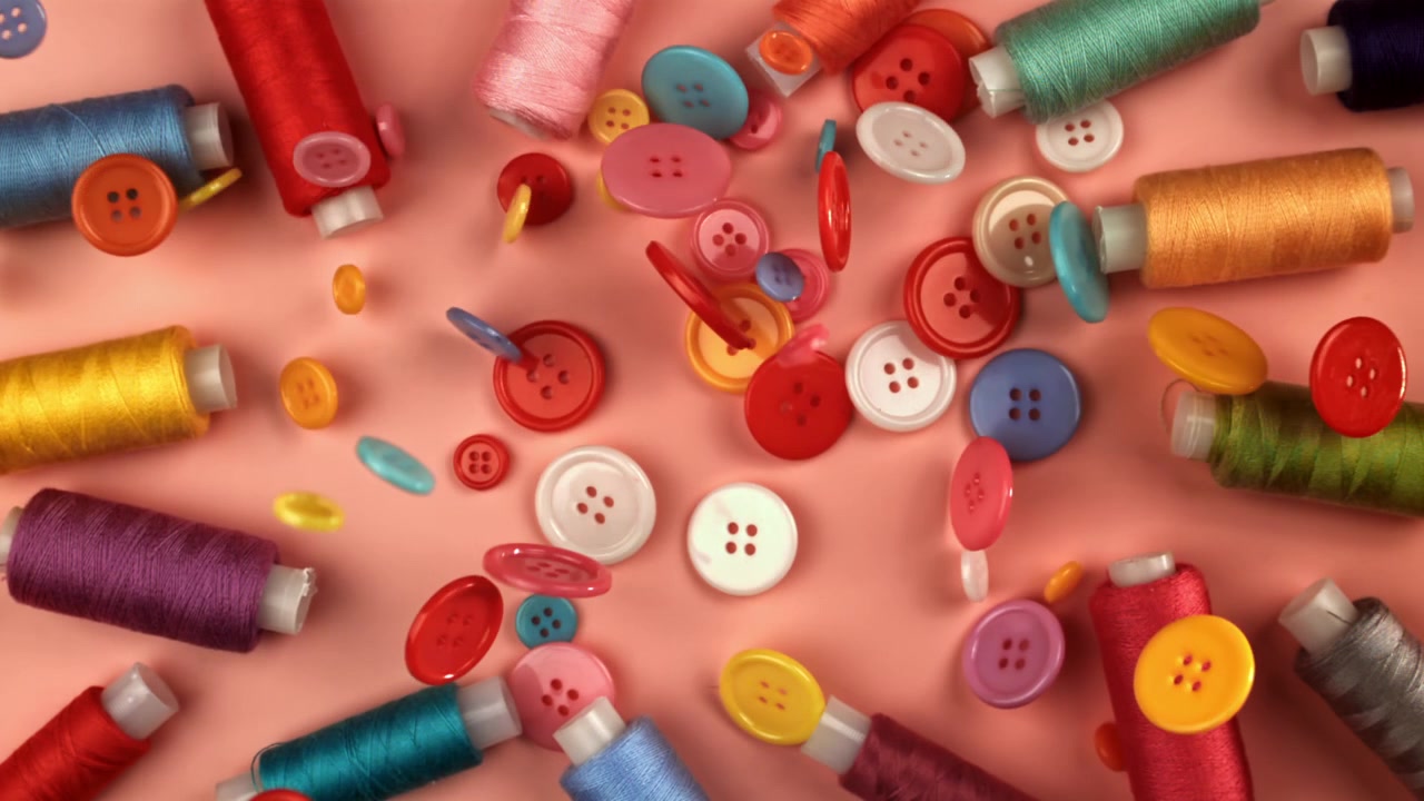 Colorful Buttons and Thread Spools Falling on Pink Background