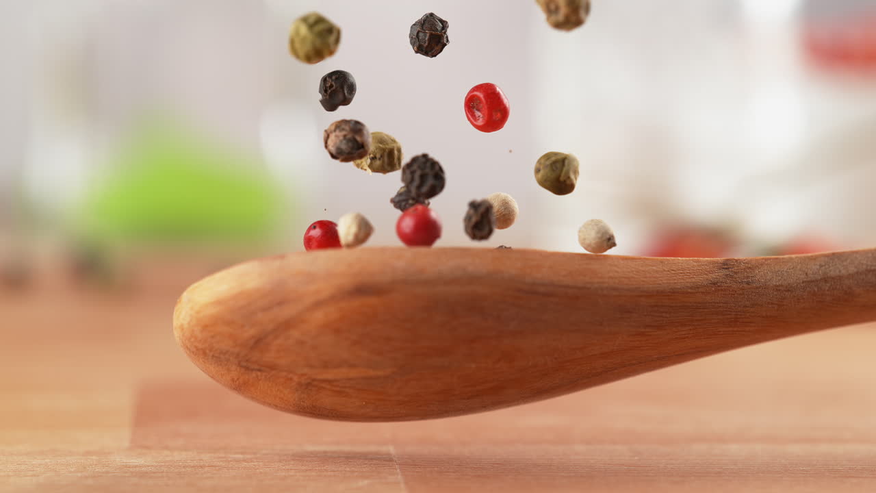 cuchara de mezcla de pimienta multicolor cae sobre la mesa y la especia se dispersa en macro y cámara lenta