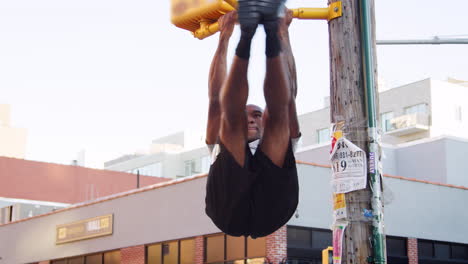 Young black man doing pull ups from crossing light in street