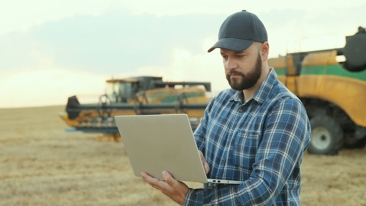 Succesful farmer working on laptop computer and looking at harvesting machines