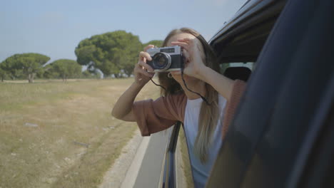 ragazza che fotografa con la fotocamera attraverso la finestra della macchina aperta