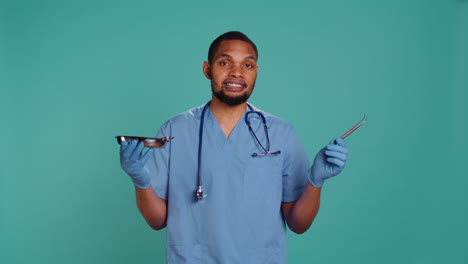 Male-nurse-in-scrubs-holds-medical-tools,-explaining-use