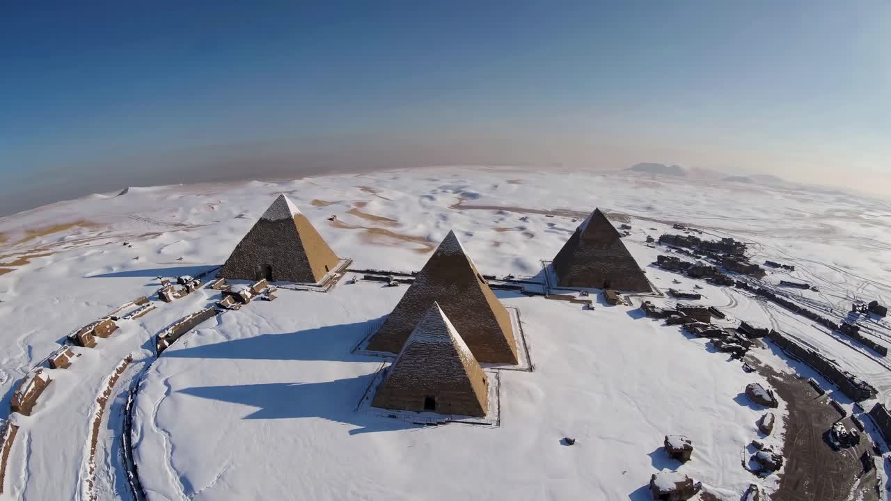 Aerial video shot of snow-covered pyramids in a vast desert landscape, showcasing a surreal blend