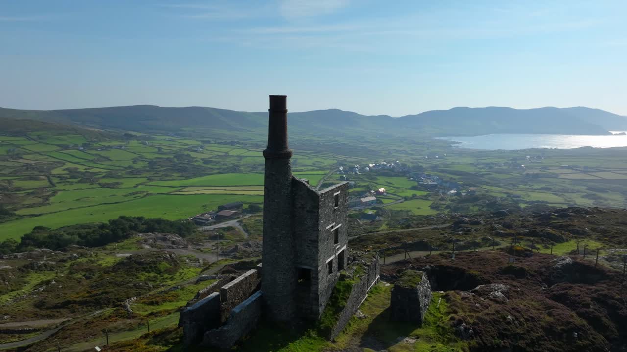 Copper Mine, Allihies, County Cork, Ireland, September 2024. Drone orbits clockwise around the ruined structure with the North Atlantic Ocean in the distance and sunlight reflecting under a blue sky.