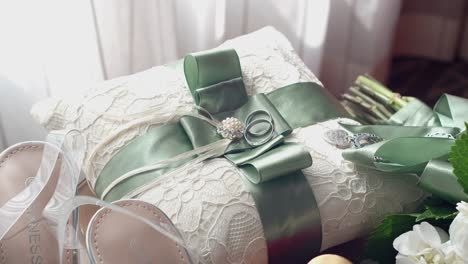 two white gold wedding rings on a pillow with green ribbon, on a wooden table