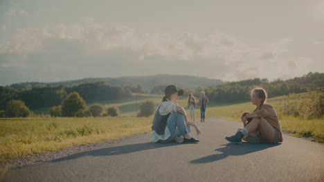 friends sitting together on footpath by meadow