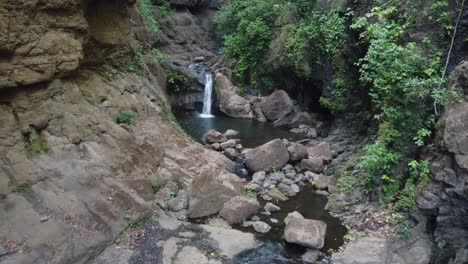 Canyon-aerial-flies-up-narrow-rock-grotto,-waterfalls-flow-into-pools