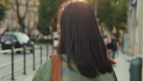 back view on the young pretty brunette woman in glasses and with red lips walking the street in stylish outfit, then turning to the camera and laughig cheerfully