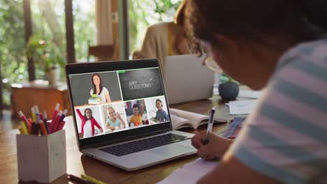 Schoolgirl-using-laptop-for-online-lesson-at-home,-with-diverse-teacher-and-class-on-screen