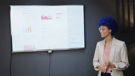 biracial casual businesswoman with blue afro making presentation in office, slow motion