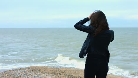 Junge-Frau-Berührt-Brünettes-Haar,-Das-Sich-Beim-Spaziergang-Am-Sandstrand-Im-Wind-Bewegt