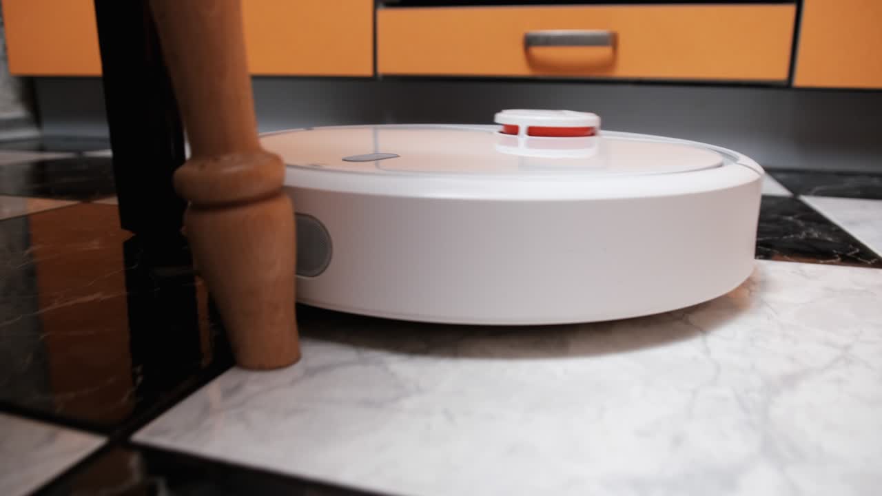 The Robot Vacuum Cleaner Cleans in the Modern House on the Tiles Floor at Kitchen