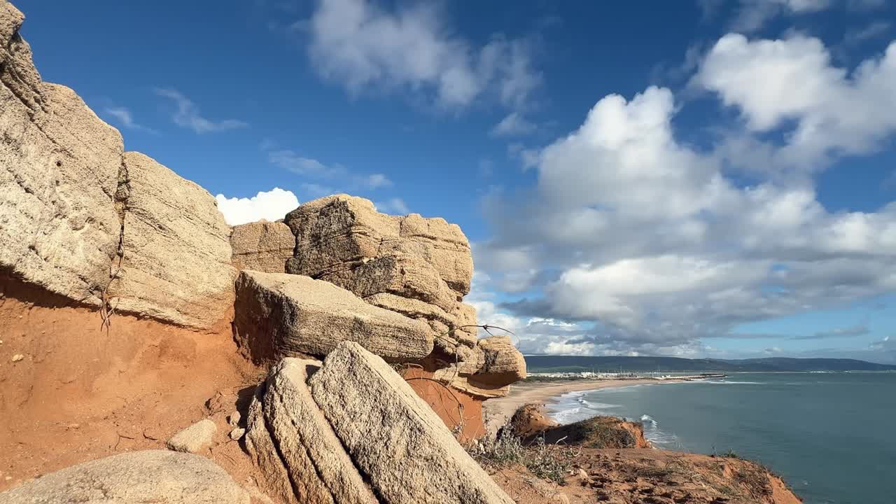 Ripresa timelapse statica di nuvole in rapido movimento sopra scogliere rocciose a Barbate Cadice con onde che si infrangono lungo la costa atlantica.