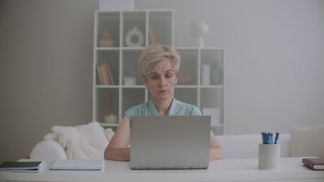 aged woman is sitting at home and chatting online by laptop with internet connection talking with friend