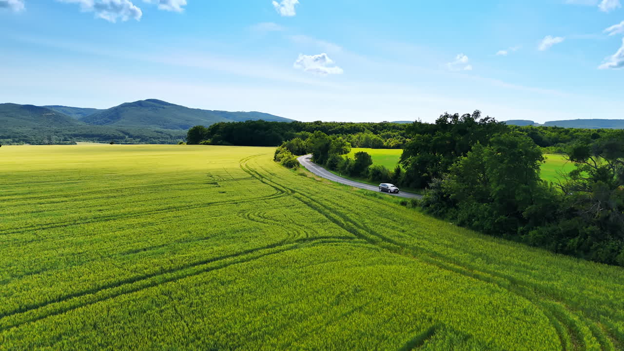 Flight over the beautiful green fields near the highway. Lush forests and verdant mountains at backdrop. Aerial view.