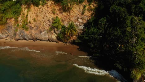 Vista-Aérea-De-Una-Modelo-En-Bikini-En-Una-Playa-Junto-A-Un-Acantilado-Disfrutando-De-Las-Olas