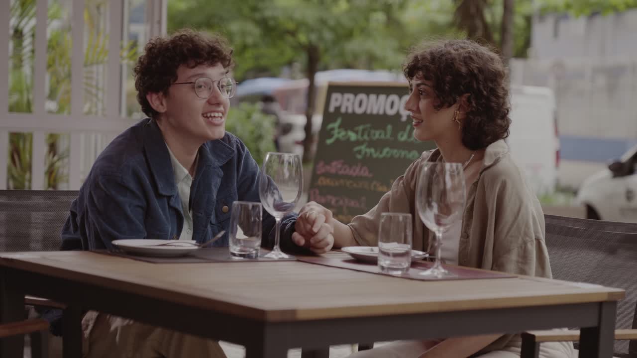 Young Adults Holding Hands and Conversing at an Outdoor Restaurant