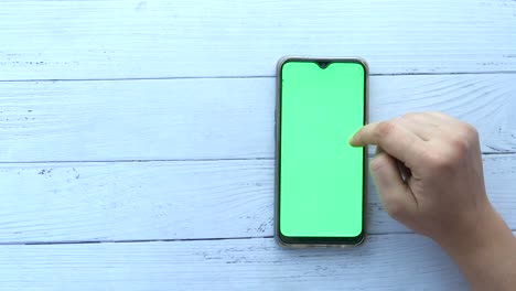 hand touching a smartphone with a green screen on a wooden table