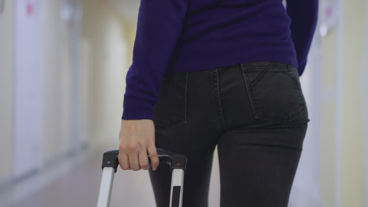 여자 가 호텔 의 복도 에서 여행 가방 의 손잡이 를 들고  ⁇ 고 있다