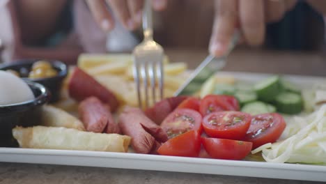 a plate of food with sausages, tomatoes, and cucumber