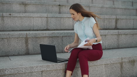 Businesswoman-working-with-business-papers-on-street.-Employee-typing-on-laptop