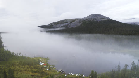 Vista-Aérea-De-Un-Lago-Lleno-De-Niebla-Que-Se-Acerca-A-Una-Persona-Que-Rema-En-Un-Bote