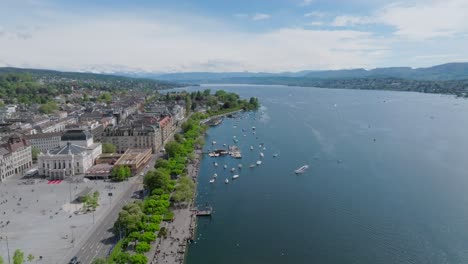 Fast-forward-moving-drone-shot-showing-Zurich-opera-house,-city-inhabitants,-transport,-skyline-and-the-lake-front