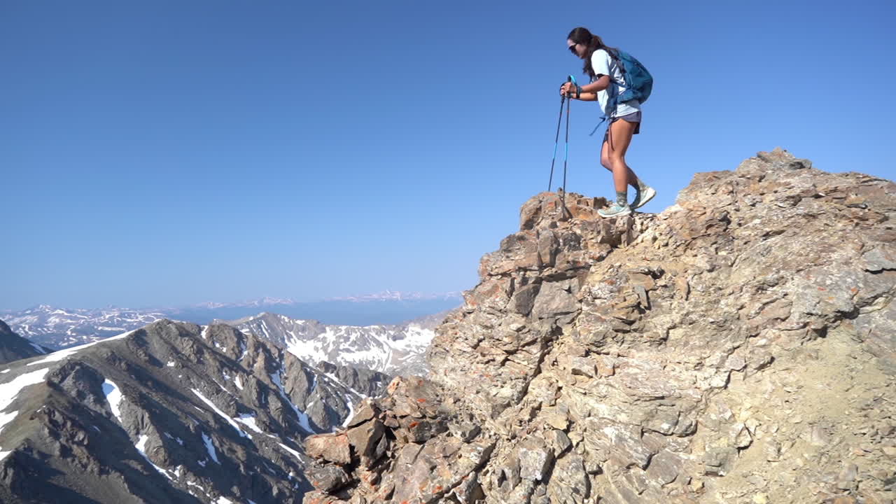 montañero femenino en la cima de la cumbre rocosa caminando cuidadosamente con bastones de trekking