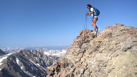 female mountaineer on top of rocky summit walking carefully with trekking poles