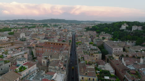 Buildings-in-metropolis,-forwards-fly-above-straight-street-lined-with-old-multistorey-apartment-houses-with-rooftop-terraces.-Rome,-Italy