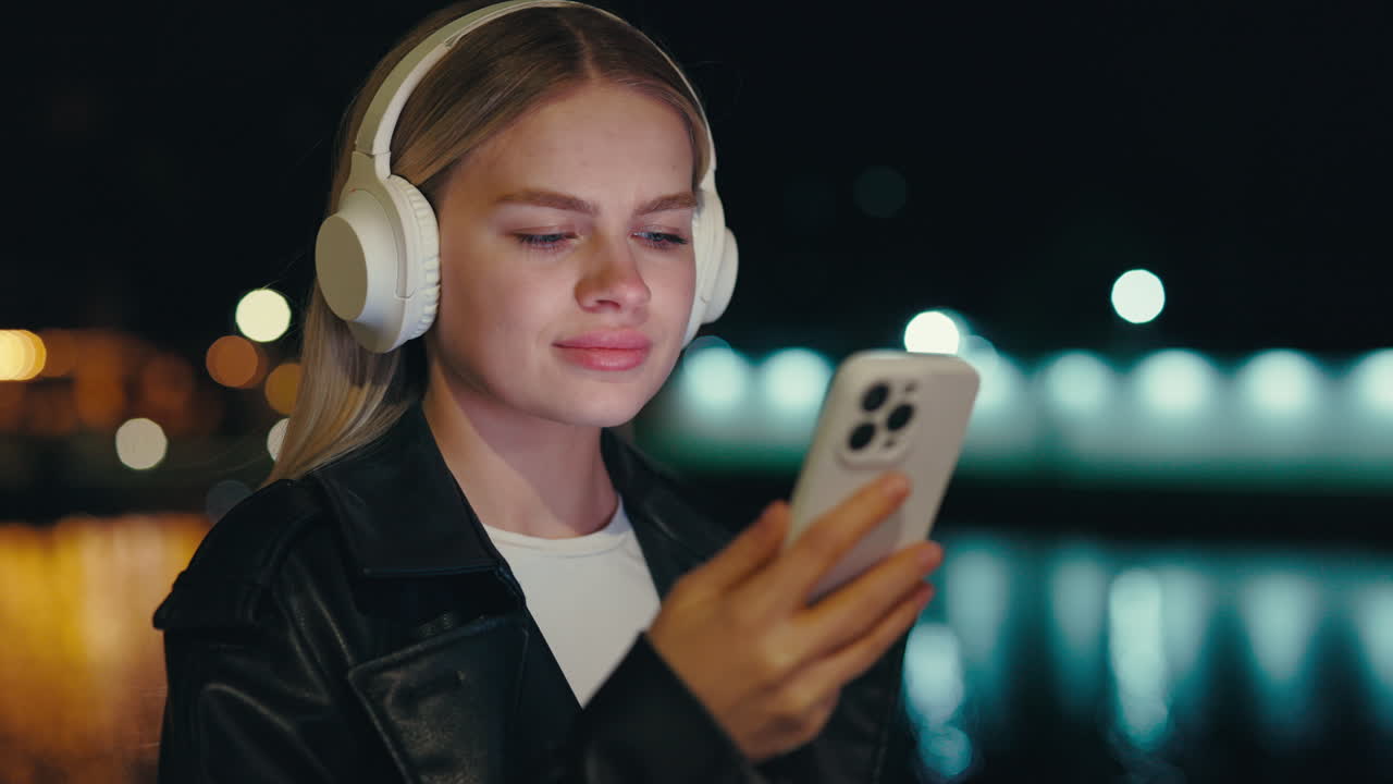 Woman using mobile phone with headphones at night