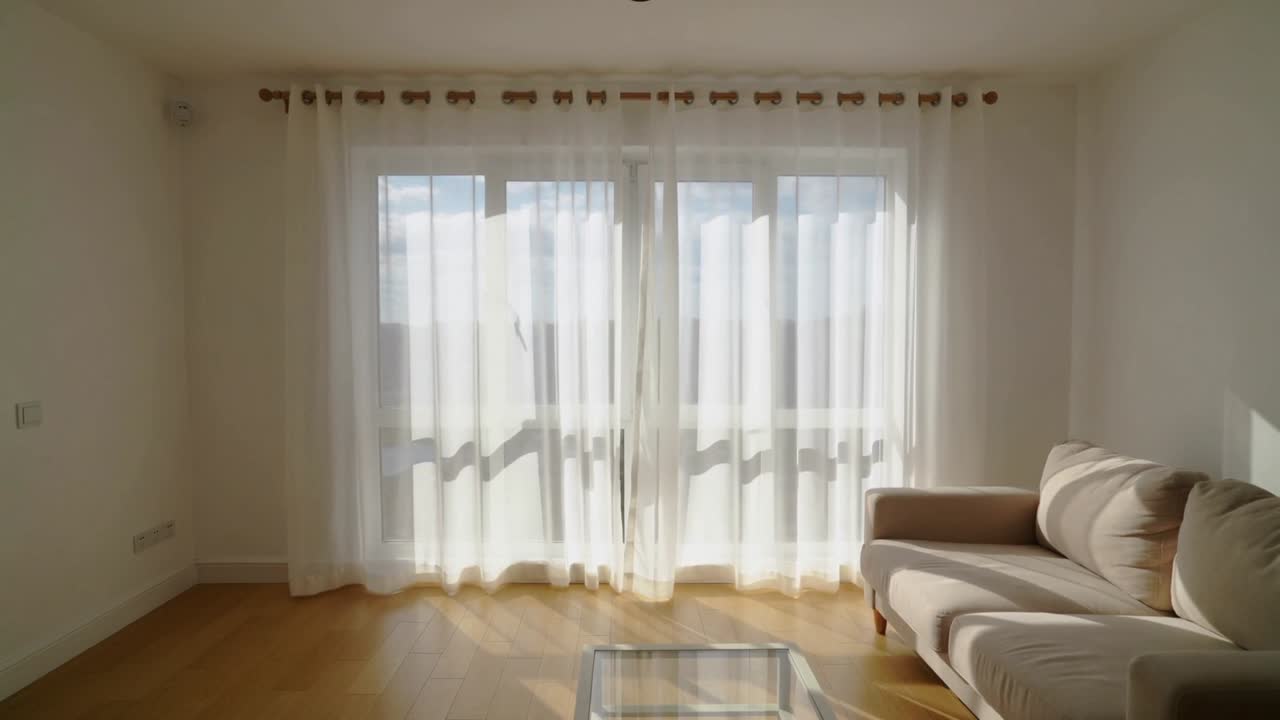 Luz solar em movimento fazendo cortinas translúcidas balançarem sobre a porta de correr de vidro e o chão na sala de estar.
