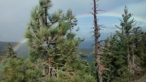 a colorful and bright rainbow lighting up a dark grey sky on the way to emerald bay state park in lake tahoe, california