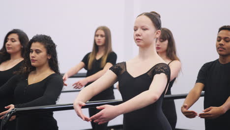 male and female students at performing arts school rehearse ballet with teacher in studio