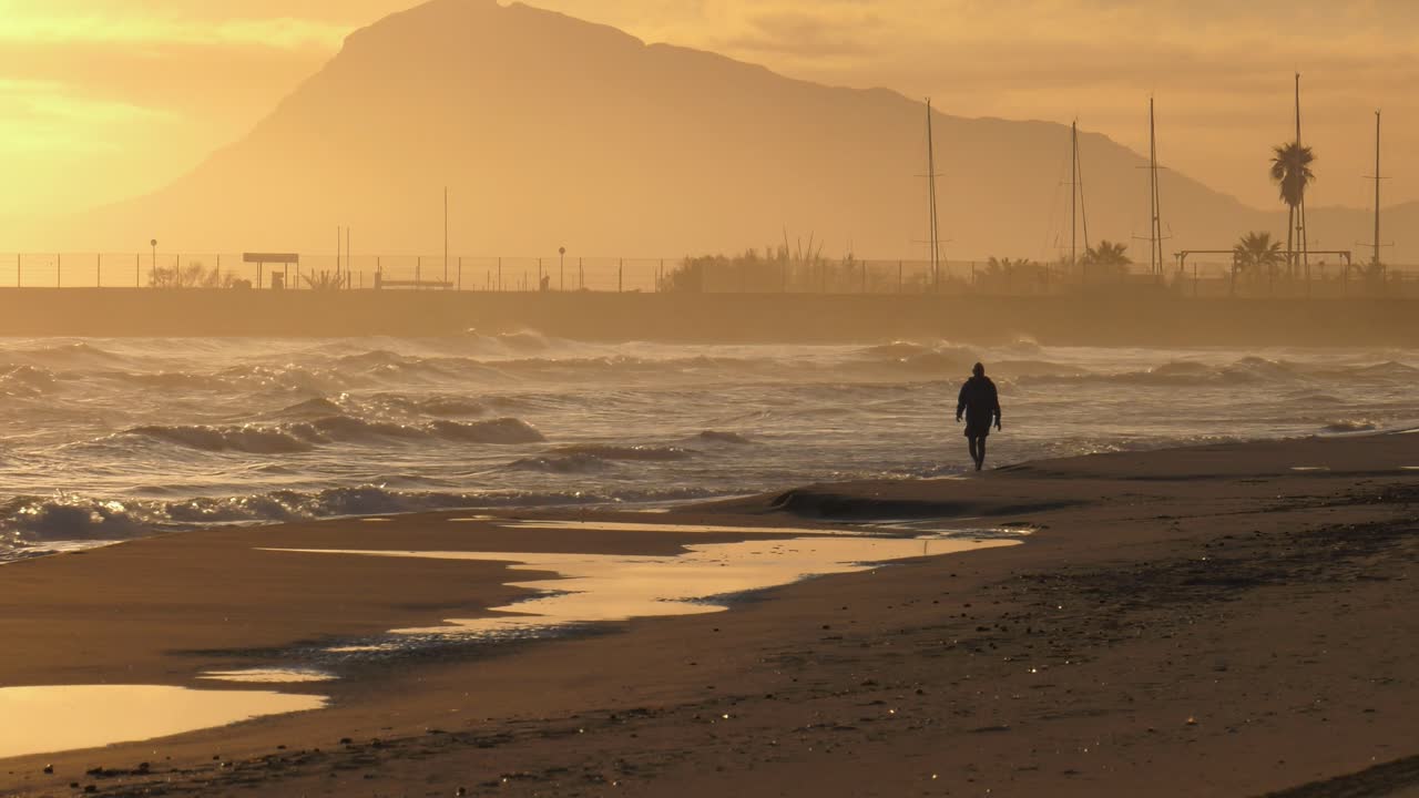 playa de arena al amanecer con un anciano caminando por la orilla, montaña en el fondo, gran tiro