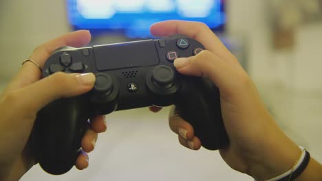 Primer-Plano-De-Manos-Femeninas-Usando-El-Controlador-Dualshock-Ps4-Negro-Para-Jugar-Dentro-De-Casa-Con-Tv-En-Segundo-Plano