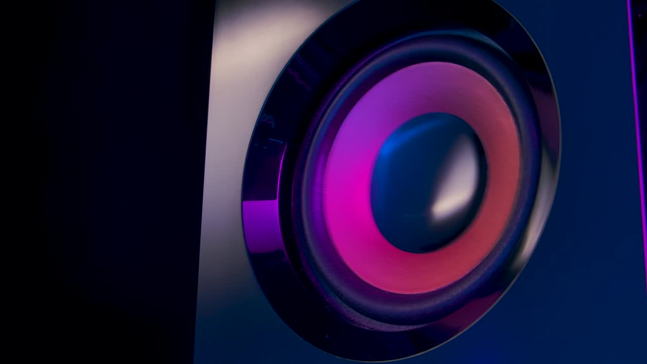Moving subwoofer close up. Speaker part. Black membrane lit by colorful neon club lights. Concept of musical instrument. Close up. Slow motion
