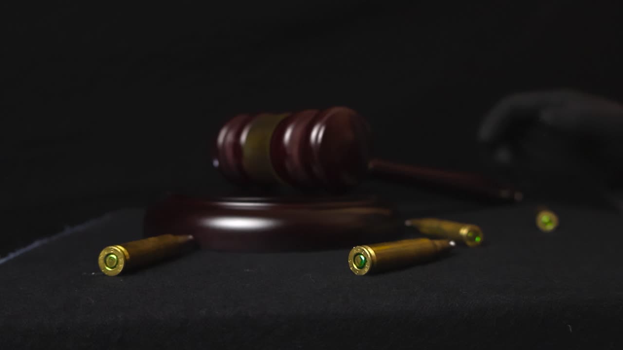Wooden brown court hammer or gavel mallet hitting on a wooden board and making high caliber ammo ammunition bullets fly in the air that are around the hammer. Black background and gloved hand swinging
