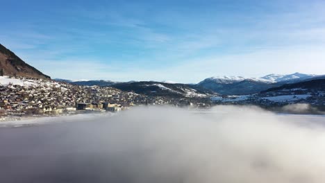 voss morning aerial flying through frost haze above vangsvatnet lake while looking at town of voss with mountains and blue sky background