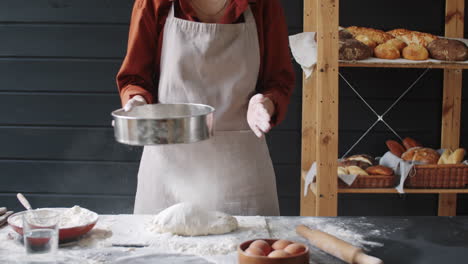 female baker sifting flour while preparing dough