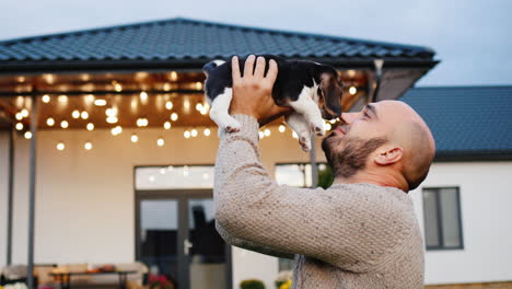 Un-Hombre-De-Mediana-Edad-Juega-Con-Un-Cachorro-Beagle-En-El-Fondo-De-Su-Casa.-Lo-Sostiene-En-Sus-Manos-Y-Lo-Lanza