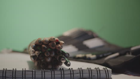 Putting-pile-of-colorful-crayons-on-paper-notebook,-greenscreen-in-background