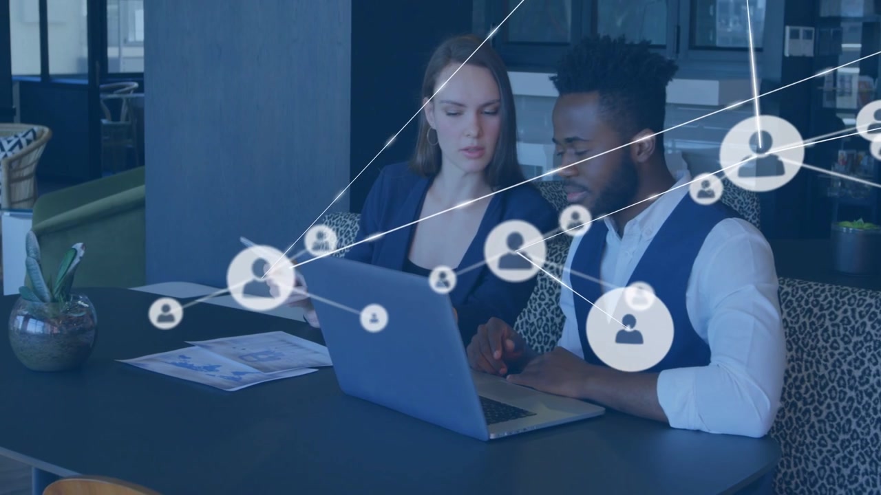 Woman holding tablet and man pointing at laptop in lobby, sparking growing business network overlay