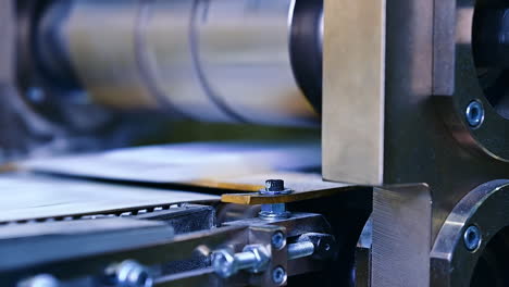 strong bolts and internal screws holding a construction of a machine for producing diapers. a large rotating horizontal shaft over the conveyer belt blurred at the backdrop..