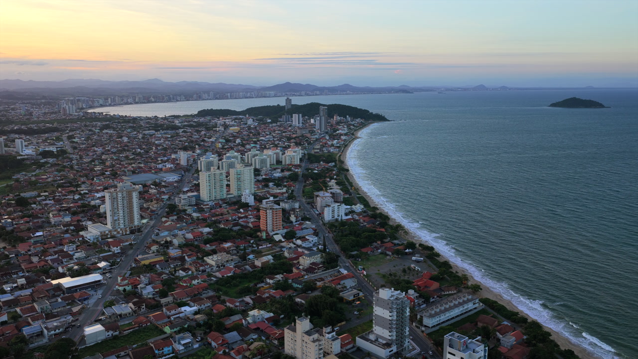City and beach of Penha and Piçarras during the late afternoon after a tropical sunset. Aerial descent.