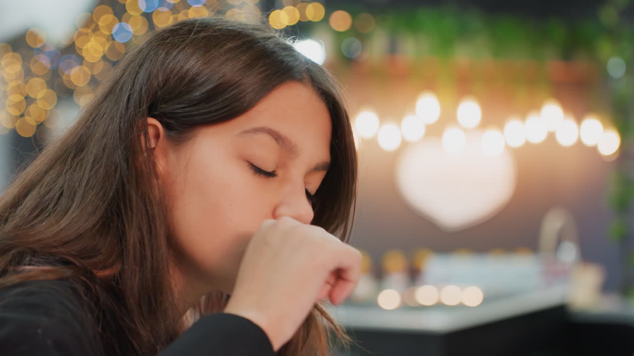 Studentessa che studia in un bar accogliente con luci bokeh calde a forma di cuore, scena serale con bagliore soffuso e aroma di caffè, penna e quaderno in mano, scrive e disegna concentrata, rilassata e determinata